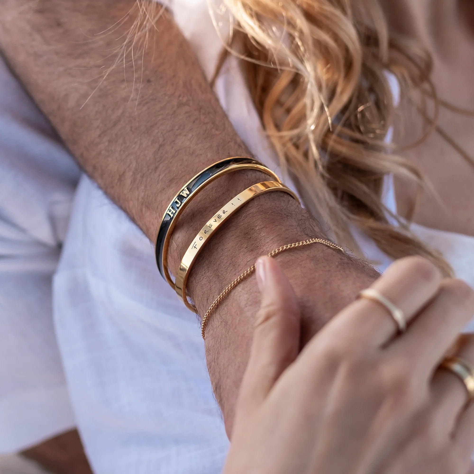 Close-up of a person's arm with multiple gold bracelets and rings.