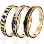 Three gold-tone bangle bracelets with inlay patterns, displayed on a reflective white surface. The bracelets feature zebra print, marbled black and white, and tortoiseshell inlay designs, with 'FLORENCE LONDON' engraved on the inside.